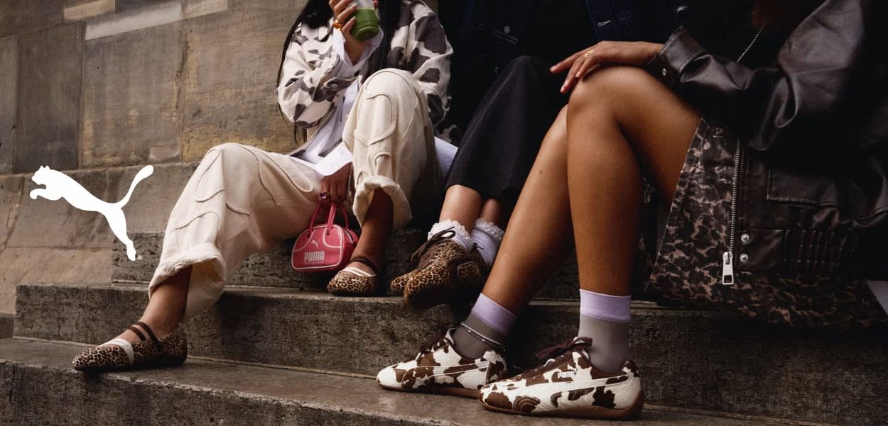 Trzy osoby siedzą na kamiennych schodach. Mają na sobie różne obuwie: baleriny w leopardzie wzory i brązowe buty w krowie plamy. Casualowy styl ubioru.