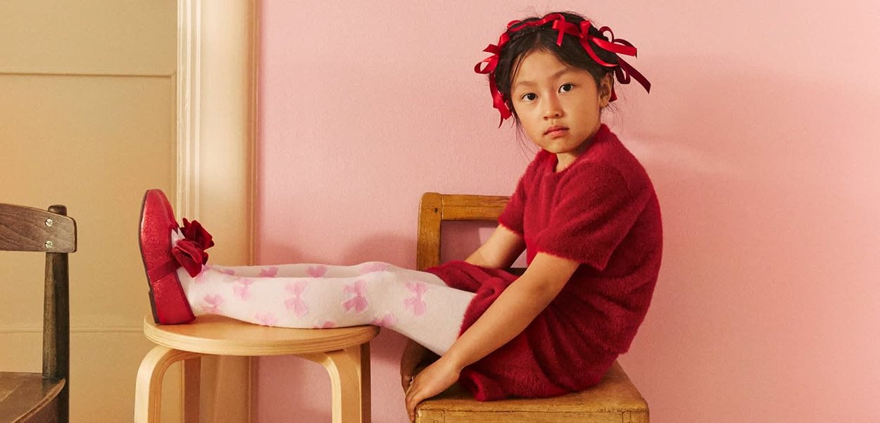 Red fuzzy dress and matching red shoes with a bow, paired with white stockings featuring pink bow patterns. Background is light pink.