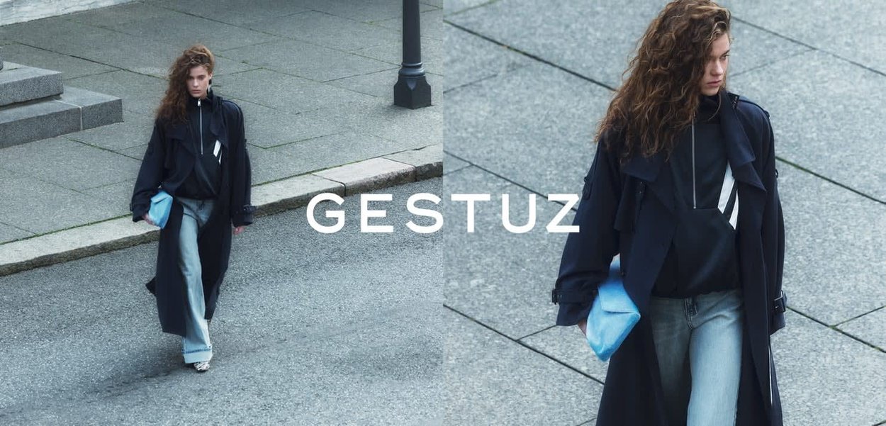 Kvinde går på betontrappe iført sort trenchcoat, sort top, lyseblå jeans og holder en lyseblå clutch-taske.