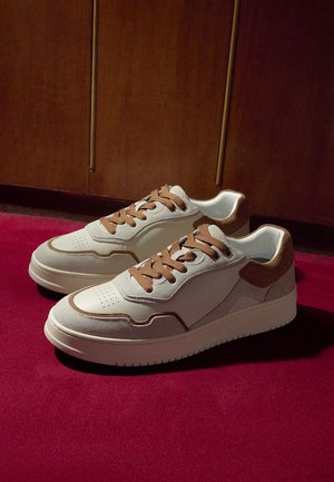 Sneakers bianche con dettagli marroni, realizzate in suede e pelle, design con lacci, punta traforata e suola in gomma.