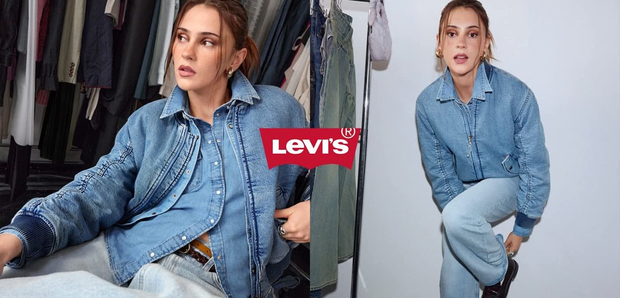 Frau trägt Jeansjacke und Jeans und posiert drinnen, mit sichtbarem Levi's-Logo in der Mitte des Hintergrunds.