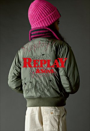 Green bomber jacket featuring embroidered text "REPLAY & SONS" in red. Includes various stitched designs and a ribbed hem. Paired with a pink knit beanie.