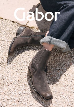Brown suede ankle boots with a fitted shape, side zipper, and a slight heel. Features a smooth texture and stitched detailing along the sides.