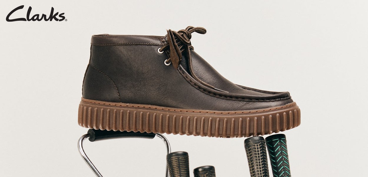 Braune Lederstiefel von Clarks mit dickem geripptem Absatz, die auf einem Metallsessel mit gemusterten schwarz-grünen Griffen vor einem schlichten Hintergrund stehen.