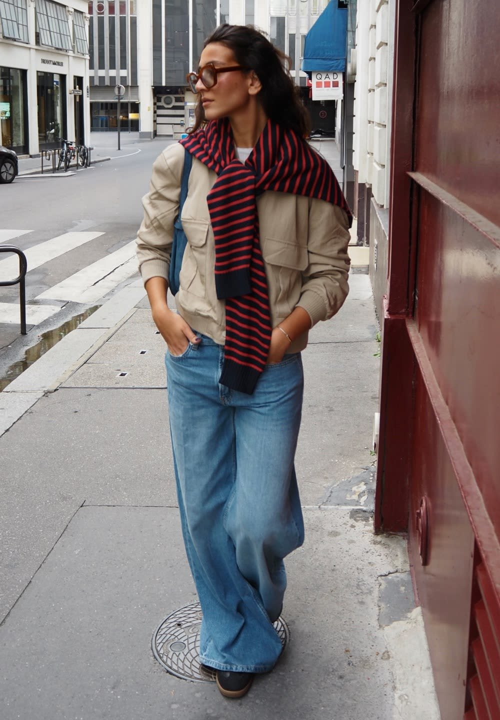 Beige jacket with large pockets, paired with wide-leg light blue jeans. Worn with a red and navy striped scarf, walking on city street.