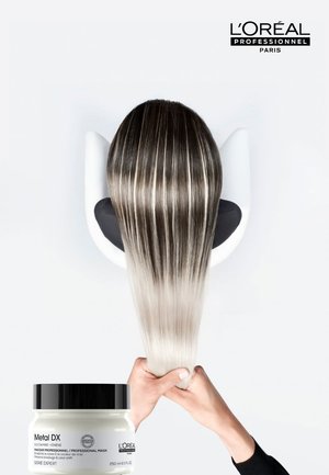 Langes, glattes Haar mit dunklen Ansätzen, die zu platinblond verblassen, gehalten von Händen über einem Glas der L'Oréal Metal DX Haarmaske.