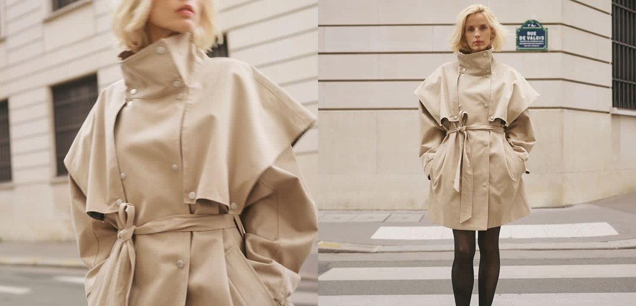 Blonde Frau trägt beigen, übergroßen Trenchcoat mit Gürtel und schwarze Strumpfhosen, steht auf einem Zebrastreifen in der Stadt.