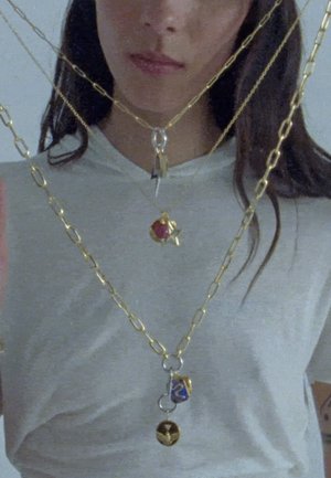 Collares de metal dorado con varios colgantes, incluyendo una gema roja, una estrella y un encanto azul y dorado, superpuestos sobre una camiseta gris clara.