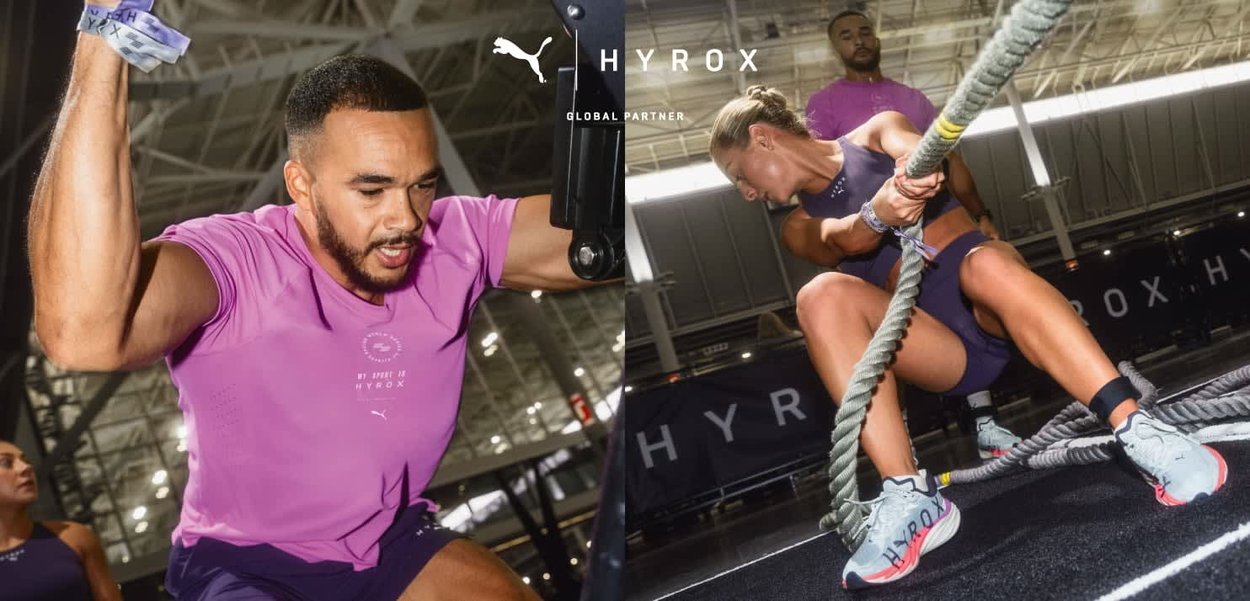 Hombre y mujer realizando ejercicios intensos con cuerda y resistencia en un gimnasio con marca HYROX y un entrenador personal observando.