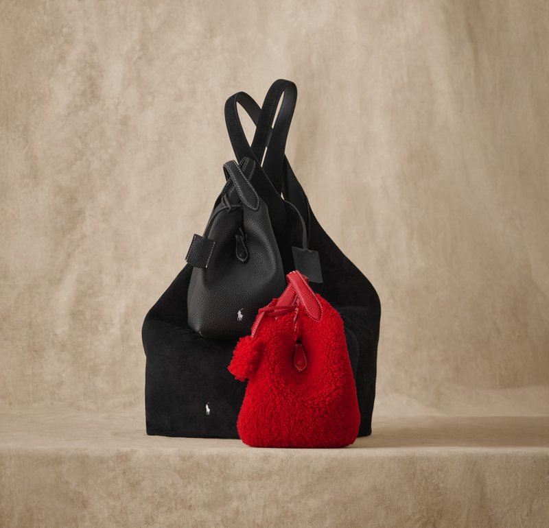 Kaksi laukkua pinottuna: teksturoitu musta mokkalaukku ja pieni punainen pörröinen laukku, jossa on tupsuyksityiskohta, molemmissa on logokoristeet.