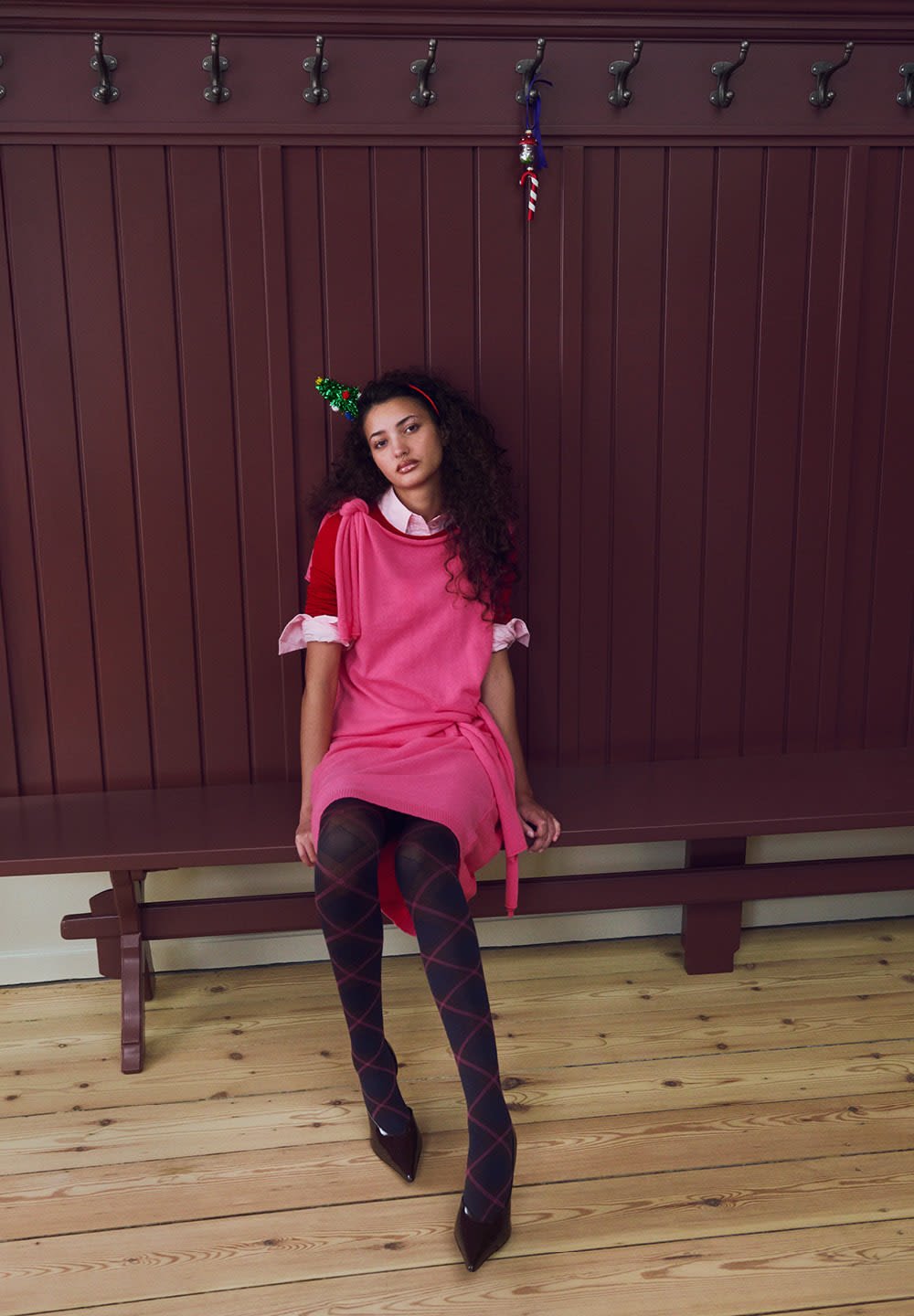 Rosa stickad klänning med korta ärmar, rosa krage över en vit skjorta, svart- och röd diamantmönstrad strumpbyxa och bruna spetsiga högklackade skor.