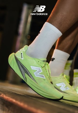 Neon green New Balance sneakers with a sleek, aerodynamic design, featuring white accents and reflective detailing on the heel.