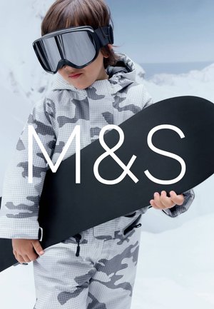 Dziecko w szarym kombinezonie narciarskim w kamuflażu i dużych czarnych goglach trzymające czarny snowboard na zaśnieżonych górach.