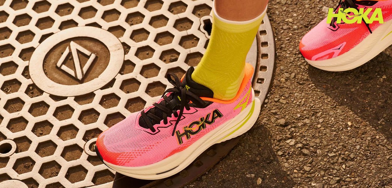 Pink and black running shoe with a textured mesh upper, featuring a yellow sole and vibrant accents, resting on a patterned metal grate.