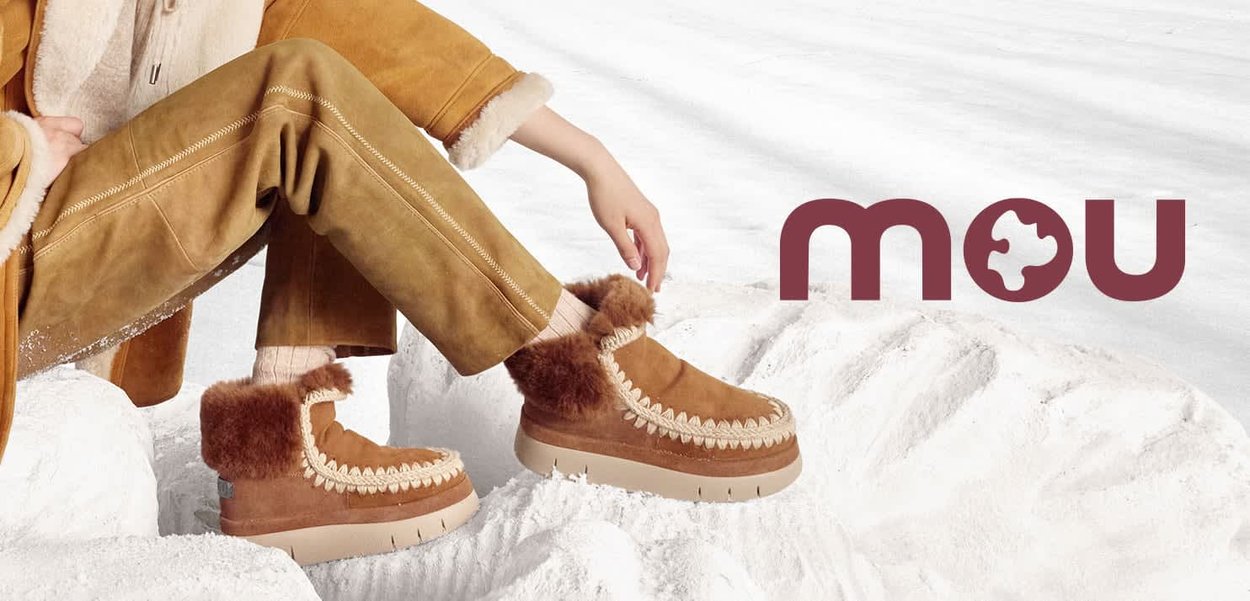 Botas de tobillo de ante marrón con ribetes de piel de pelo y costura decorativa, con una suela de plataforma gruesa. Logo "mou" mostrado a la derecha.