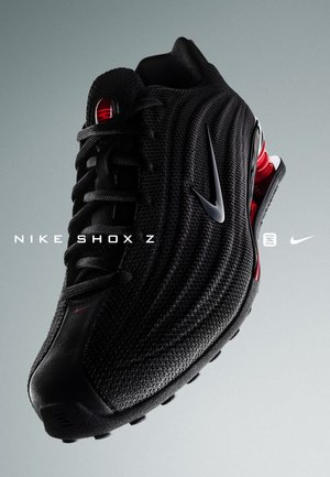 Zapatilla Nike Shox Z en malla negra con una superficie texturizada, que presenta acentos rojos y un destacado sistema de amortiguación en el talón.