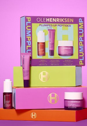 Skincare set includes a maroon oil bottle, a purple lip treatment tube, and a pink moisturizer jar, displayed on colorful boxes with logos.