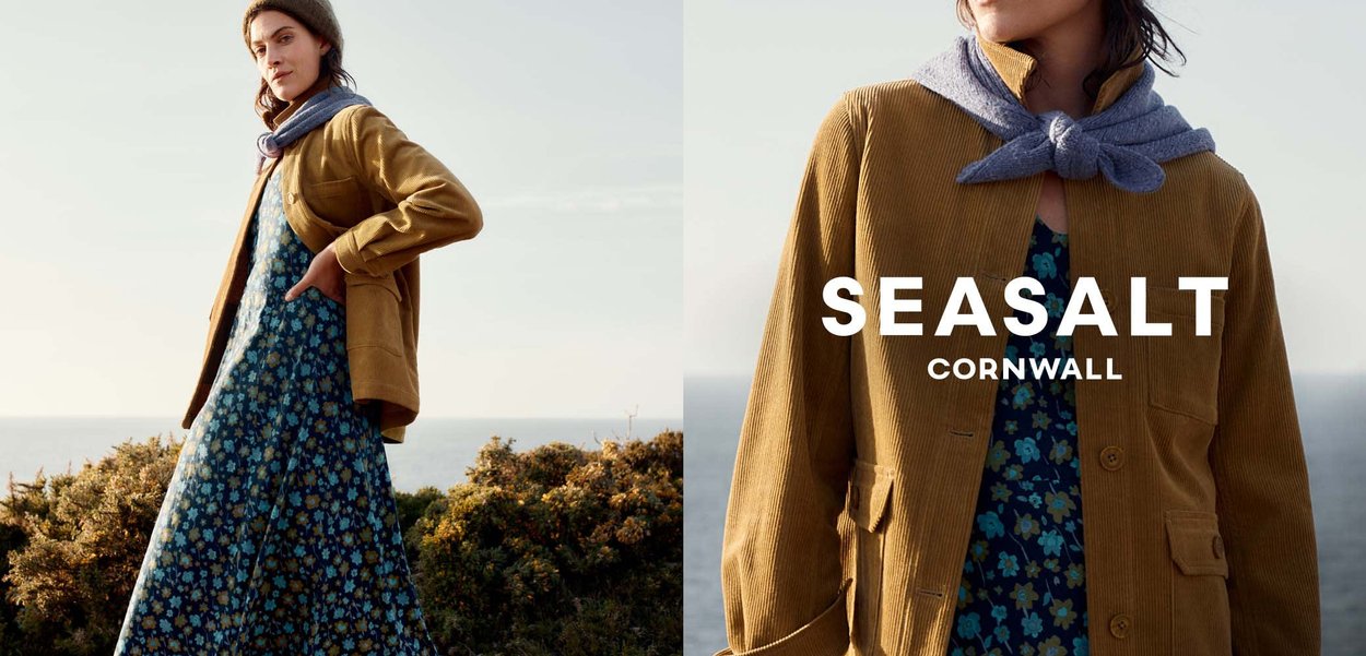 Gul fløjljakke over en blå blomsterkjole, suppleret af et gråt tørklæde og en strikket hue, sat mod et naturligt landskab.