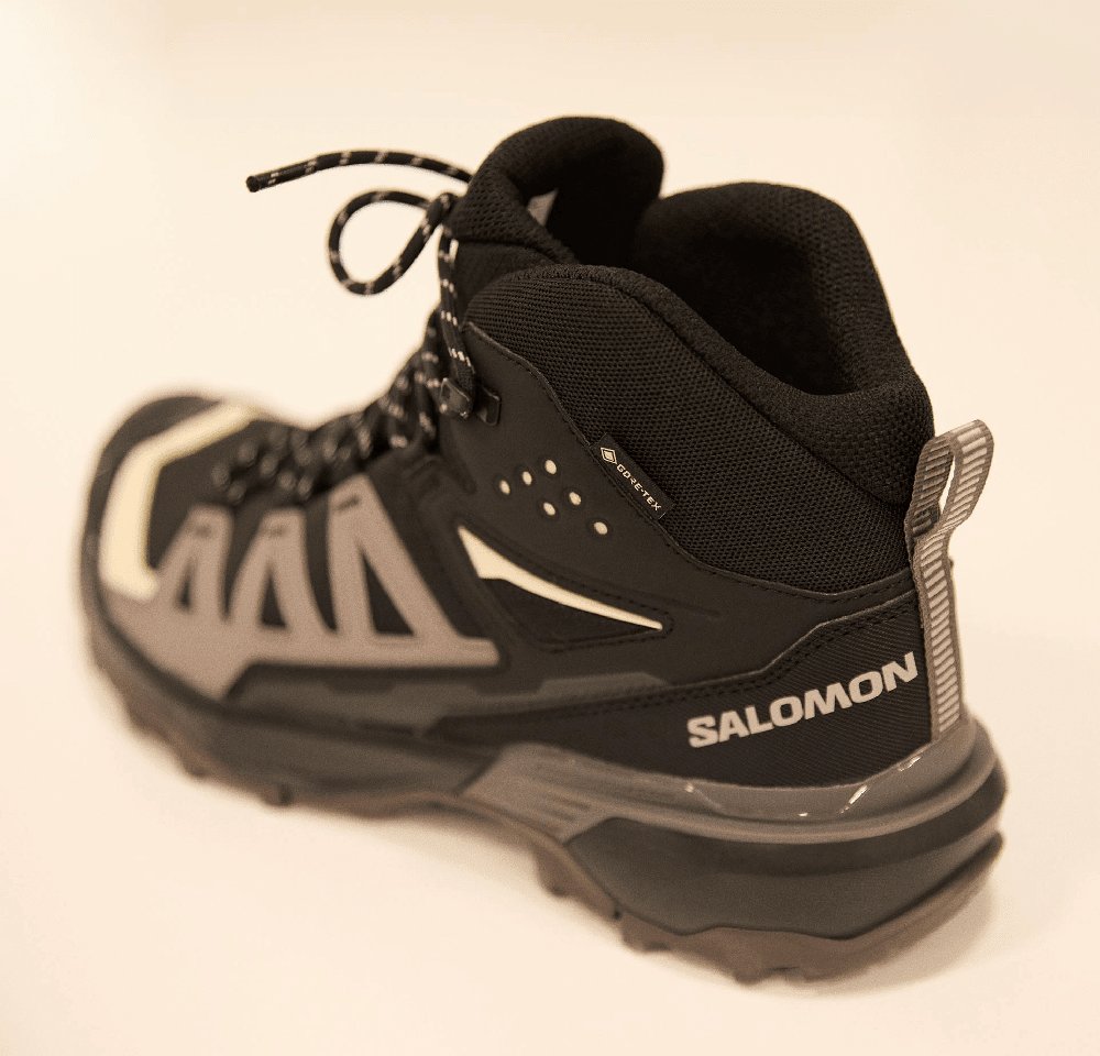 Black hiking boot with gray accents, textured fabric, reinforced toe, and lacing system. Features a Gore-Tex label for waterproofing.
