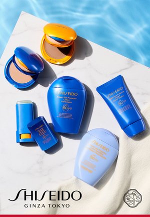 Prodotti solari assortiti Shiseido con SPF 50+, tra cui lozione, crema, stick e polveri compatte, esposti su una superficie bianca vicino all'acqua.