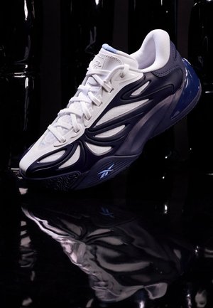 Baskets athlétiques blanches et bleu marine flottant au-dessus d'une surface noire réfléchissante avec un fond abstrait noir.