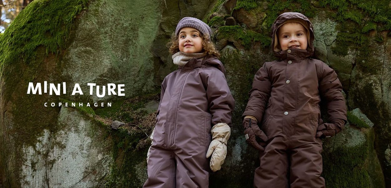 Brown insulated snowsuits with hoods, zipper fronts, and visible snaps. Gloved hands, one child wearing a knitted hat. Mossy rock background.
