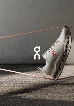 Scarpa da ginnastica bianca con accenti rossi, caratterizzata da una tomaia texturizzata, una suola ammortizzata e sezioni ritagliate lungo la base per una migliore traspirabilità.