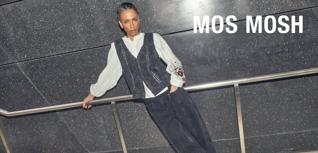 Black knit vest with intricate patterns over a white collared shirt, paired with dark textured pants, set against a dark surface.
