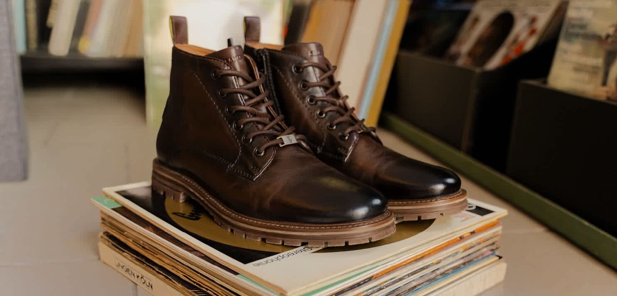 Braune Leder-Schnürstiefel mit runder Zehenpartie, kontrastierenden helleren Sohlen und einer strukturierten Oberfläche, präsentiert auf gestapelten Schallplatten.