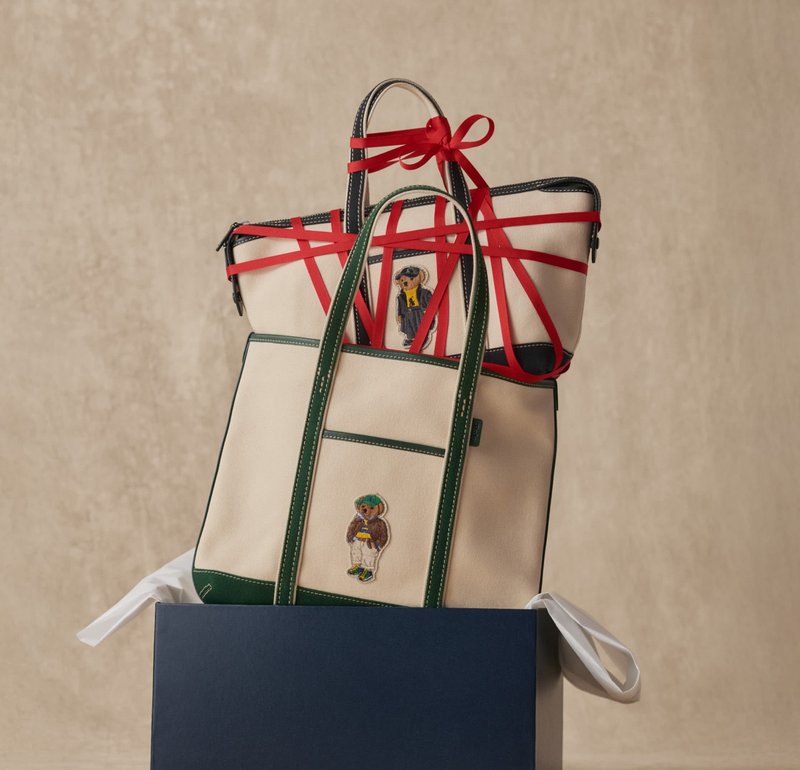 Deux sacs fourre-tout en toile beige avec des bordures vertes et noires, décorés de patches d'ours en peluche ; un sac a un ruban rouge enroulé autour des poignées.