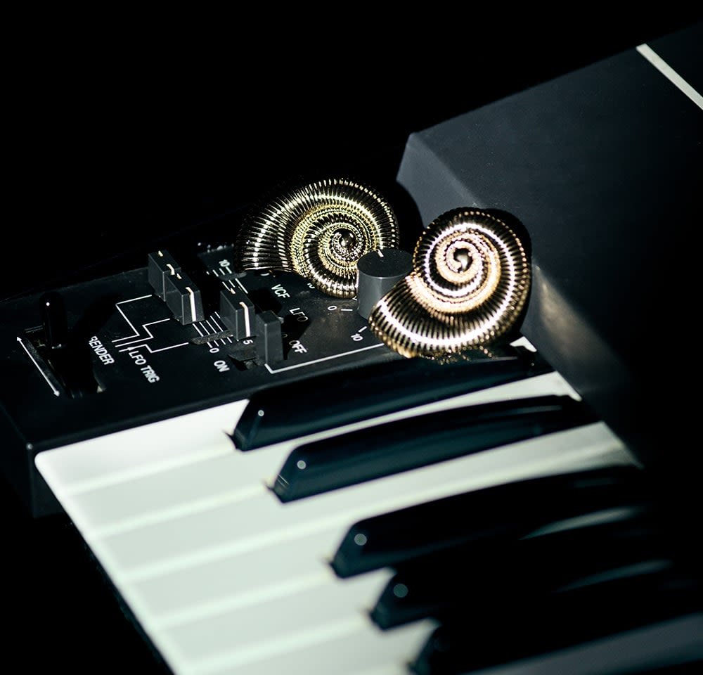 Juodas sintetinio garso klaviatūra su blizgiomis baltomis klavišais, turinti metalinius spiralinius mygtukus auksinėmis ir sidabrinėmis tonacijomis tamsiame valdymo panele.