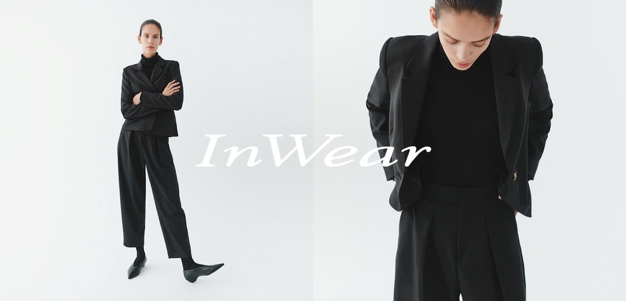 Schwarzer, maßgeschneiderter Anzug mit einem strukturierten Blazer und weit geschnittenen Hosen. Glatte Textur, minimalistisches Design, ergänzt durch ein eng anliegendes schwarzes Oberteil.