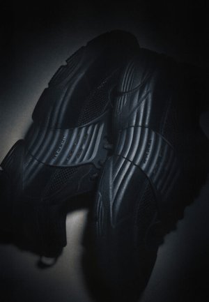 Paire de chaussures de sport noires avec semelles texturées et tissu en maille sous un éclairage tamisé.