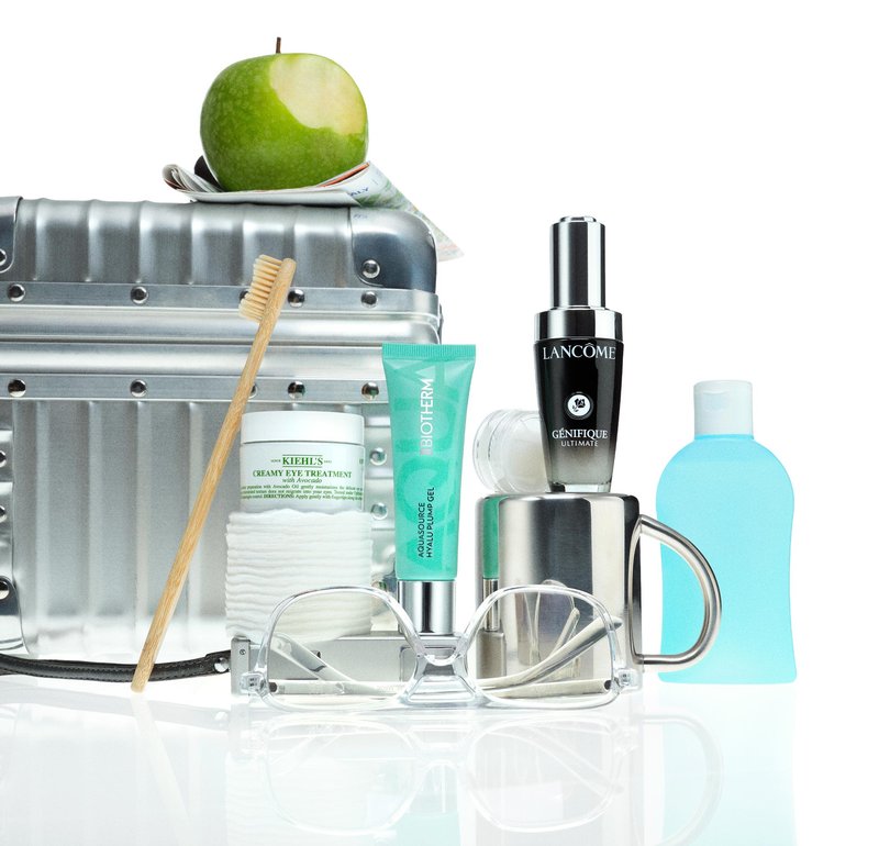 Argent métallique trousse de voyage, pomme verte, brosse à dents, lunettes transparentes, bouteille bleue, sérum noir et tube de crème verte sur une surface réfléchissante.