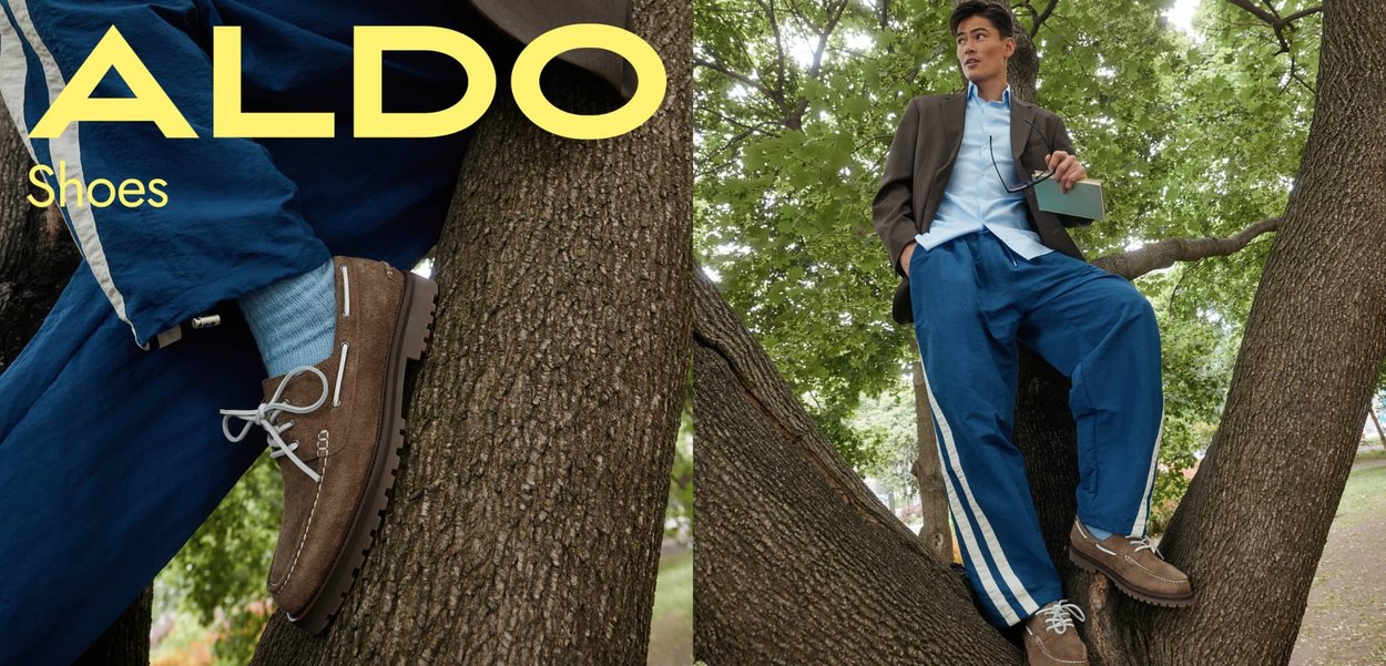 Scarpe in pelle scamosciata marrone con accenti bianchi e suole grigie, abbinate a pantaloni blu con righe bianche, sullo sfondo di un albero.