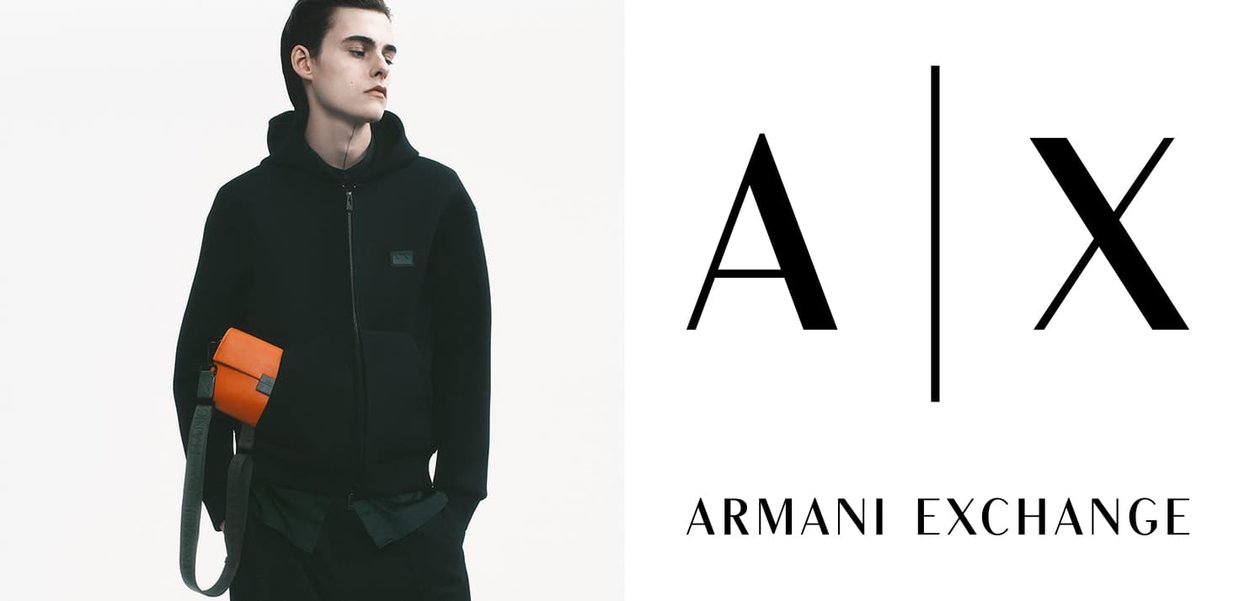 Nero zip-up hoodie con polsini a coste, abbinato a una borsa a tracolla arancione. Sfondo bianco, con il logo dell'Armani Exchange.
