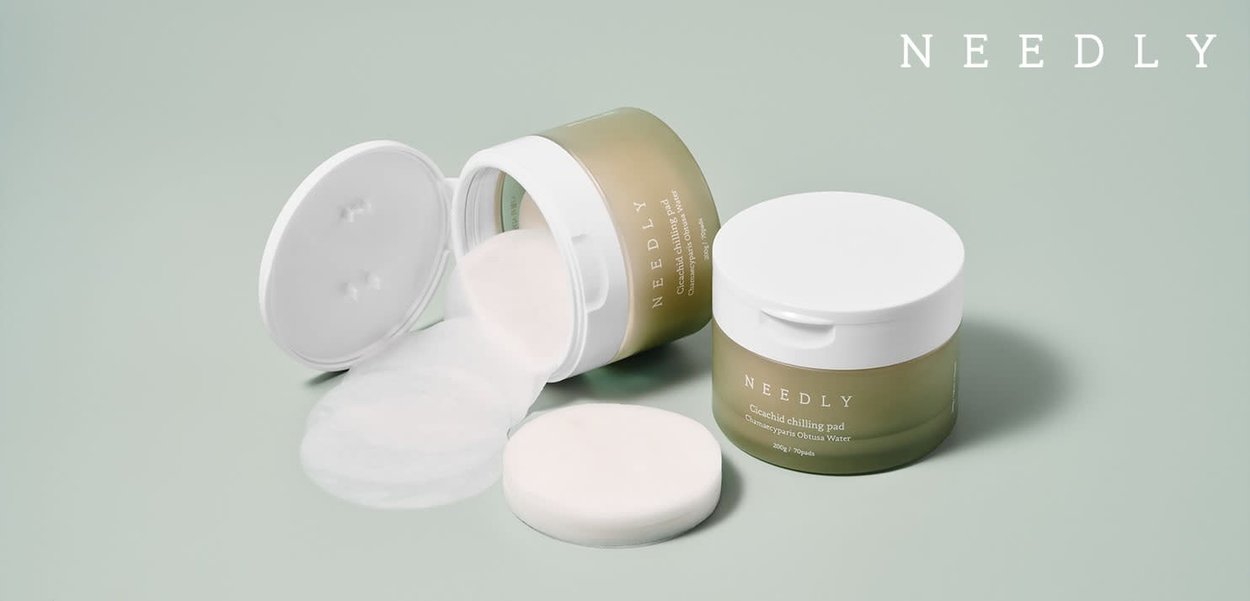 Due barattoli trasparenti di Needly Cicachid Chilling Pads, uno aperto con le piastrine che fuoriescono. I barattoli hanno coperchi bianchi e una base verde tenue.