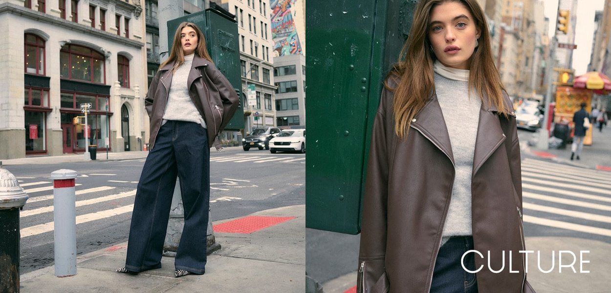 Veste de moto en cuir marron sur un pull gris clair, portée avec un pantalon en denim large foncé. Le décor montre des éléments de rue urbaine.