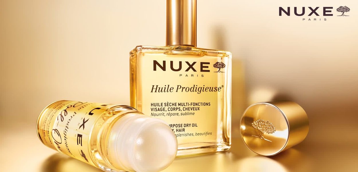 Bouteille de NUXE Huile Prodigieuse en verre transparent doré avec un bouchon doré ; présente un texte sombre et un logo en forme d'arbre. Le fond est d'un doré flou.