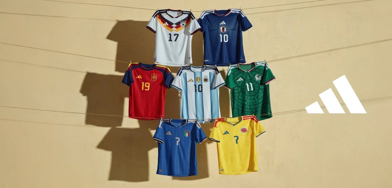 Sette maglie nazionali di calcio appese a una corda contro un muro beige con il logo Adidas sul lato destro.