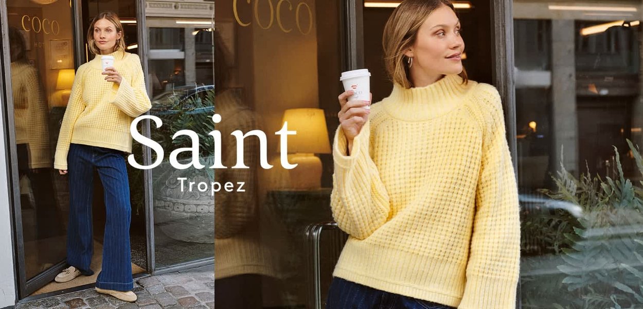 Gelber, übergroßer, strukturierter Strickpullover mit hohem Kragen, kombiniert mit dunkel gestreiften, weit geschnittenen Hosen. Das Model hält eine Kaffeetasse.