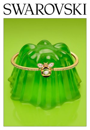 Gouden Swarovski-armband met een bij-vormige bedel met heldere kristallen, tentoongesteld op een groen gelatinevorm tegen een groene achtergrond.