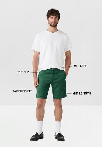 Bermudas verdes de corte medio con cremallera y ajuste entallado, combinadas con una camiseta blanca y zapatos negros. Diseño de longitud media, fabricadas en un tejido de algodón casual.