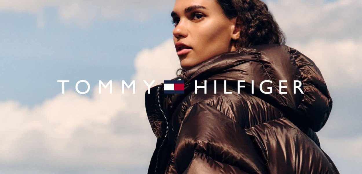 Chaquetón marrón con acabado brillante y detalles de costura visibles. Cuenta con un alto cuello y cremalleras, con el logo mostrado abajo.