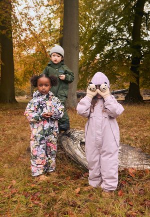 Tre børn i farverigt vintertøj: snowsuit med blomsterprint, olivengrøn parka og lyserød snowsuit med dyrehandsker. Efterårsindstilling.