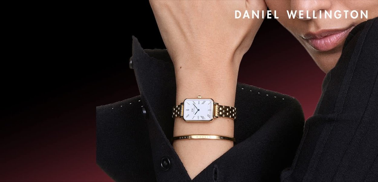 Złoty zegarek z kwadratową, białą tarczą i rzymskimi cyframi. Posiada złotą metalową bransoletę na ogniwa. Nosi się go z eleganckim czarnym strojem i ozdobną bransoletką.