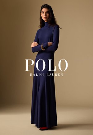 Robe longue bleu marine avec un col haut, des manches longues et une jupe évasée. Présente une texture lisse et des chaussures rouges contrastantes. Accent bracelet doré.