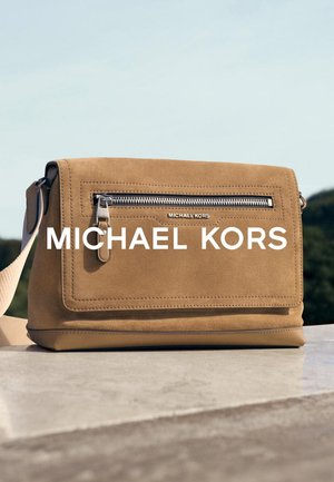 Beige semsket skinn crossbody-veske med en frontlomme med glidelås, flat design og justerbar stropp; har sølvfarget metall og logodetaljer.