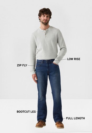 Camiseta henley gris de manga larga con tres botones, combinada con vaqueros azul acampanados que cuentan con cierre de cremallera y diseño de longitud completa.