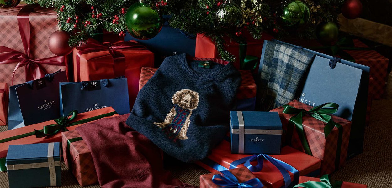 Jersey azul marino con un diseño detallado de un perro, rodeado de regalos envueltos en rojo, verde y azul con lazos, colocado bajo un árbol de Navidad decorado.